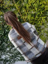 Chaqueta corta con estampado a cuadros en tonos negro, gris y marrón, con ribetes en marrón y cierre frontal con lazos.