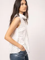 Blusa blanca sin mangas, con cuello alto con volados y detalles bordados con motivos florales.