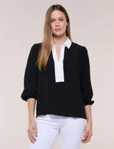 Blusa negra de calce suelto y caída ligera con sutil textura, cuello camisero blanco, escote en V con pechera en contraste y mangas tres cuartos abullonadas con puños elásticos.