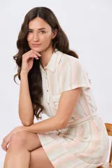 Vestido corto de lino con diseño de rayas verticales en tonos rosado, celeste, verde y beige. Presenta cuello camisero, mangas cortas, cierre frontal con botones y un lazo ajustable en la cintura.