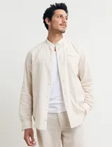 Camisa de cuello mao y manga larga, confeccionada en una mezcla de lino y algodón. Presenta un diseño de corte recto con botones en tono natural y un bolsillo pequeño en el pecho.
