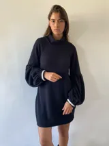 Vestido corto de tejido tipo waffle en color negro, con cuello alto, mangas largas abullonadas y puños con detalle de tejido en contraste blanco.