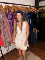 Vestido corto de tela brillante con escote en V profundo, tiras para atar al cuello y detalle de ajuste cruzado debajo del busto. Presenta un diseño entallado en la parte superior y falda con volado en el ruedo.