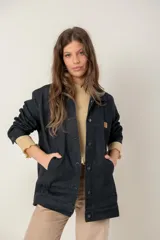 Campera de jean oversize color negro, con corte largo, cuello camisero, cierre frontal con botones metálicos y bolsillos frontales. Presenta un parche de cuero con logo en el pecho.