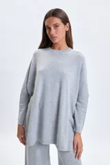 Buzo de punto oversize en color gris melange, con cuello redondo y mangas largas de corte caído.