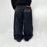 Pantalón de jean negro con efecto lavado, corte ultra baggy y bolsillos traseros con bordado de llamas blancas.