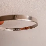 Esclava rígida de plata con diseño de cinta lisa y grabado personalizado en su cara interna.