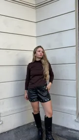 Polera de manga larga en color chocolate, confeccionada en tejido jersey térmico. Presenta un diseño ajustado al cuerpo con cuello alto y corte asimétrico en el ruedo.