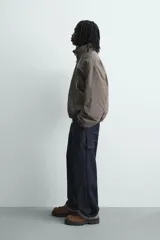 Cazadora de corte boxy fit confeccionada en tejido técnico. Presenta un diseño a rayas verticales, cuello subido, cierre frontal de cremallera y mangas largas con puños elásticos. Incluye bolsillos laterales con cremallera oculta y detalles de paneles en contraste.