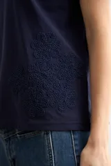 Remera azul marino de manga corta, corte recto y cuello redondo, con detalle de aplicación bordada de flores de crochet en el lateral inferior.