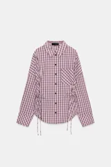 Camisa de manga larga con estampado de cuadros en tonos rosados y negros. Presenta cuello solapa, bolsillo delantero de plastrón, cierre frontal con botones y detalle de laterales ajustables con lazos.