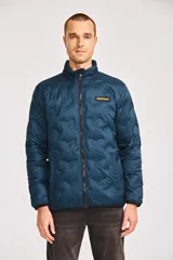 Chaqueta acolchada de peso medio en color azul petróleo, con cierre frontal de cremallera, cuello alto y parche de silicona con el logotipo de la marca en el pecho. Cuenta con bolsillos laterales y ribetes elásticos en puños y dobladillo.