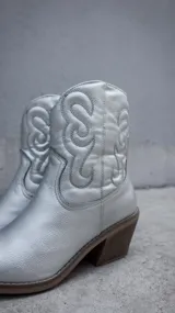 Botas texanas de caña corta en color plateado metalizado, con diseño de costuras decorativas en el lateral y taco cuadrado de madera.