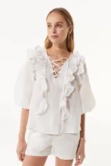Blusa blanca de tela texturizada con volados frontales, escote en V con cordones cruzados y mangas tres cuartos abullonadas.