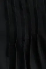 Blusa negra de tejido liviano con corte holgado, manga circular corta y escote en V con tiras finas ajustables. Presenta alforzas verticales en el frente y ojales metálicos decorativos en el escote y los bordes de las mangas.