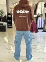 Canguro oversize marrón chocolate con capucha, bolsillos laterales y estampa en la espalda con la leyenda "Keep your HOPE alive".