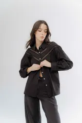 Camisa negra de algodón con detalles de encaje broderie en el pecho y mangas. Presenta cuello clásico, cierre frontal con botones y mangas largas abullonadas.