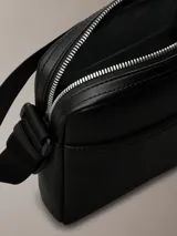 Bandolera Calvin Klein Jeans negra de poliuretano con correa ajustable, cierre superior con cremallera y logo estampado en el frente.