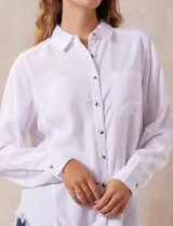 Camisa blanca de lyocell, marca Hester & Orchard. Tiene cuello con solapa, abertura central con botones, bolsillo aplicado en el pecho y ruedo desflecado.