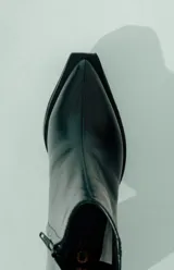 Bota corta de cuero negro, con caña media y punta cuadrada. Se caracteriza por su taco geométrico y voluminoso, con acabado texturado.