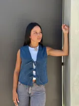 Chaleco de jean azul con cierre frontal mediante lazos ajustables, sin mangas y corte recto.