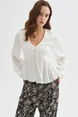 Blusa blanca de viscosa, con cuello en V, detalles de frunces en el frente, botones decorativos y mangas largas holgadas.