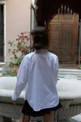 Camisa oversize de manga larga en color blanco, confeccionada en algodón. Presenta cuello clásico, puños abotonados y una abertura central ovalada con jaretas ajustables que permiten fruncir la prenda.