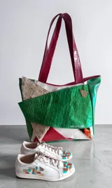 Cartera tipo tote de cuero combinada con diseño patchwork en tonos verde, bordó, beige y detalles metalizados, con doble asa de hombro y cierre superior.