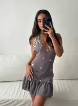 Vestido mini gris de tejido liviano, con escote halter profundo y espalda descubierta, adornado con apliques de nácar en el pecho y volado en la falda.