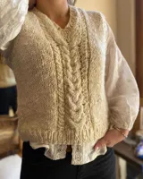 Chaleco de lana merino color crudo, tejido a mano con punto trenzado central y cuello en V.