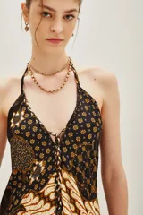 Vestido largo de corte fluido con estampado estilo batik en tonos oscuros, marrones y crema. Presenta un diseño inspirado en pañuelos con volado en el ruedo y escote en V.