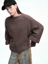 Sweater de tejido de punto color marrón con textura tipo waffle, diseño amplio, hombros caídos y cuello redondo. Presenta un bolsillo frontal aplicado y mangas con puños anchos decorados con botones.