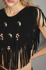 Top de cuero vacuno negro con diseño estilo navajo, caracterizado por flecos largos en todo el contorno y apliques metálicos circulares con detalles de cuentas de madera.