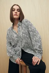 Camisa de calce relajado con estampado lineal irregular en blanco y negro. Presenta cuello clásico, abotonadura frontal, mangas largas con puños camiseros y detalles de recortes verticales en el frente.