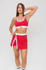 Conjunto deportivo de dos piezas color rojo con detalles en blanco. Incluye un top deportivo con cuello redondo y elástico inferior con logo, y una pollera short con tajo frontal.