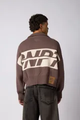 Campera tejida de punto con cierre frontal completo, cuello tipo polo y diseño con franja horizontal en contraste con estampado gráfico. Presenta puños y ruedo acanalados, con corte holgado.