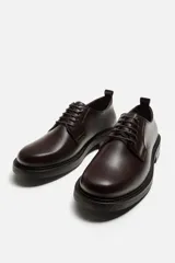 Zapato tipo blucher fabricado en piel de alta calidad, con cordonera de cinco pasados, horma redonda y suela a tono con ligero tacón.