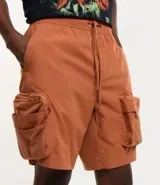 Bermuda cargo color terracota con cintura elástica y cordón de ajuste. Presenta múltiples bolsillos tácticos laterales con cierre y recortes decorativos.