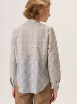 Camisa de algodón color gris claro, con cuello mao, cierre frontal de botones y mangas largas. Presenta un estampado sutil de hojas y flores, y detalles de bordado calado en los hombros.
