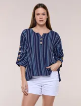 Blusa Erika de algodón con estampado de rayas en tonos azules, rosados y amarillos. Presenta cuello redondo con escote en V y botones frontales, mangas cortas decoradas con una fila de botones en los laterales y dobladillo asimétrico.