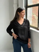 Blusa negra de manga larga con escote en V y costuras decorativas en color blanco. Presenta un corte holgado con aberturas laterales en el ruedo.