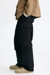 Pantalón cargo de lona de algodón con bolsillos laterales con solapa, bolsillos al bies y bolsillos traseros. Presenta pliegues en las rodillas y cierre con botón.