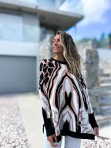 Sweater de punto con diseño oversize y estampado abstracto en tonos negro, beige y blanco. Presenta cuello redondo, mangas largas con puños ajustados y un corte holgado que cae suavemente sobre la figura.