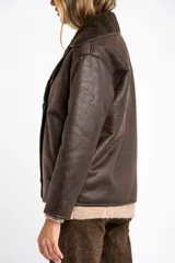 Campera tipo gamulan de corte oversize, color marrón oscuro con interior y solapas de corderito al tono. Presenta cierre frontal y mangas largas.