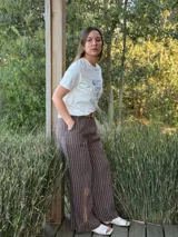 Pantalón de lino marrón con rayas verticales blancas, corte recto, cintura con elástico ancho y cinturón de rafia extraíble.