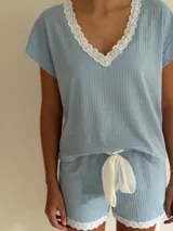 Pijama celeste de algodón acanalado compuesto por una remera de manga corta con escote en V adornado con puntilla blanca, y un short a juego con elástico y lazo de ajuste en la cintura.