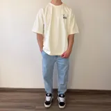 Remera oversize de algodón pesado en color blanco, con cuello redondo y moldería amplia. En la espalda cuenta con un gran parche rectangular estampado con una fotografía en blanco y negro de aves volando sobre el agua y texto tipográfico al margen.