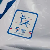 Camiseta de fútbol Umbro del Club Nacional de Football, modelo Home 2025, para hombre. Diseño blanco con sutil patrón en relieve, cuello redondo con ribetes azules y rojos, y detalles en las mangas. Incluye escudo del club, logo Umbro y sponsor Antel en el frente.