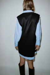 Vestido corto que combina una camisa celeste de manga larga con cuello solapa y botones frontales, con un chaleco de tejido negro sin mangas y escote en V superpuesto.