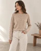 Sweater de tejido de punto color beige, con cuello redondo y cierre frontal parcial con botones. Presenta mangas largas con puños acanalados y volados sutiles.
